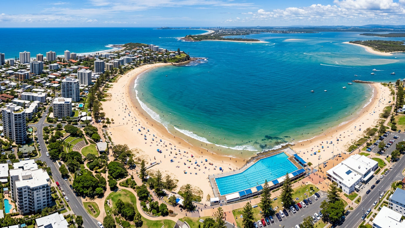 Aerial view of a coastal city with a large blue pool on a sandy beach.