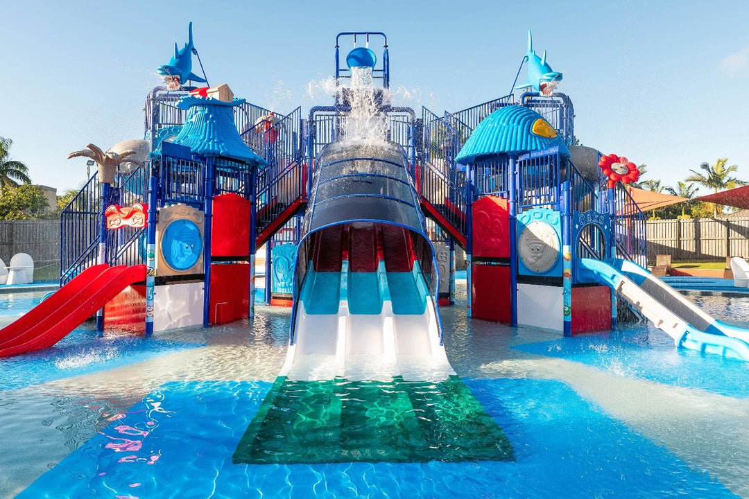 Colorful water slide and play structure in a pool area with clear blue sky.